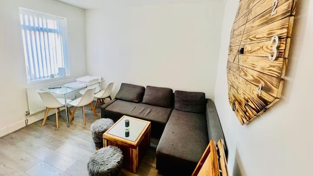 A modern living room with a sectional sofa, a glass coffee table, and a unique wooden wall art piece. - 4-bed House, Sleeps 9 w Garden & On-street Parking (Liverpool)