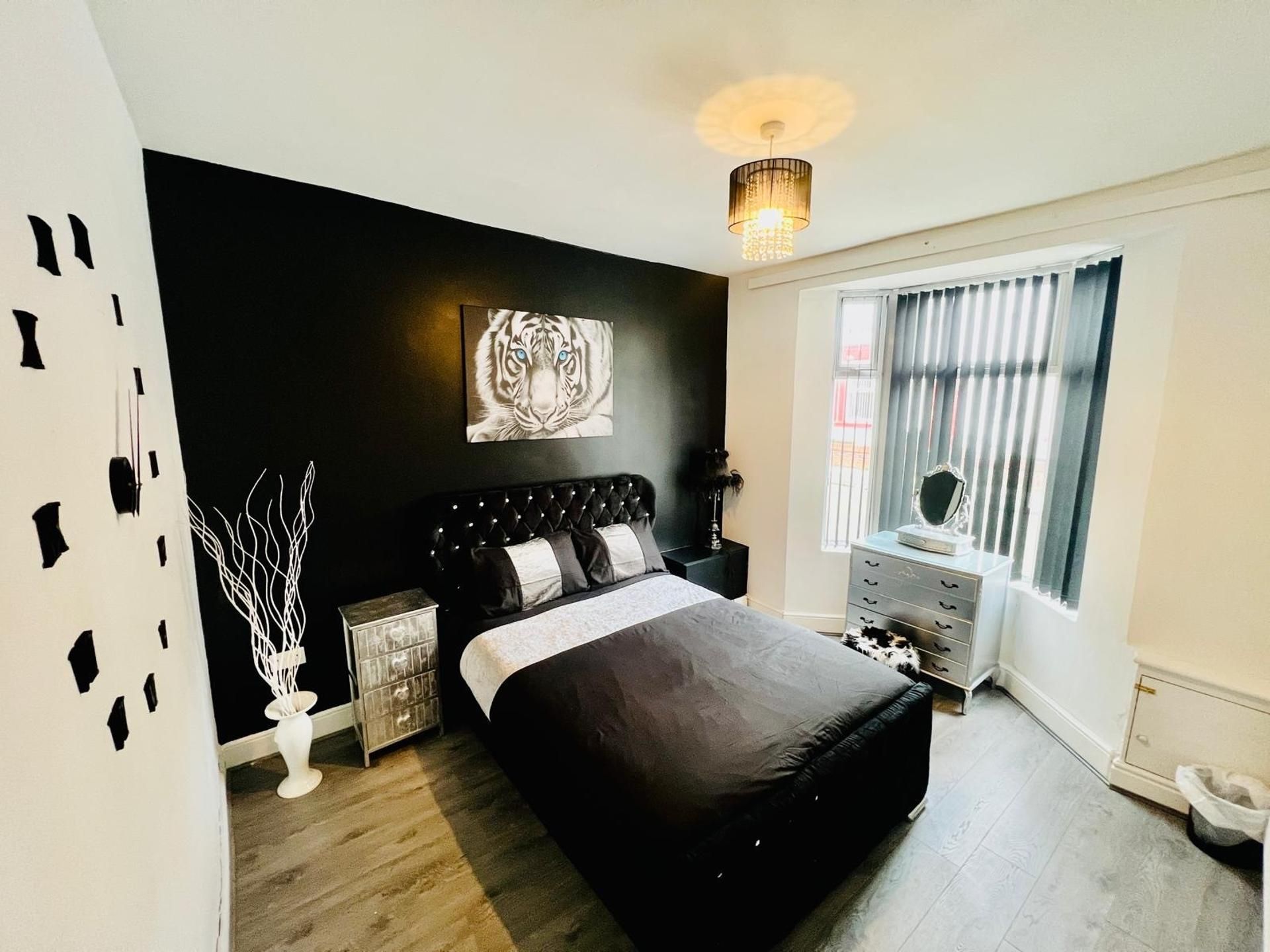 A modern bedroom with a black bed, a white vase, a small cabinet, and a painting on the wall.