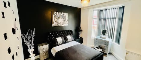 A modern bedroom with a black bed, a white vase, a small cabinet, and a painting on the wall.