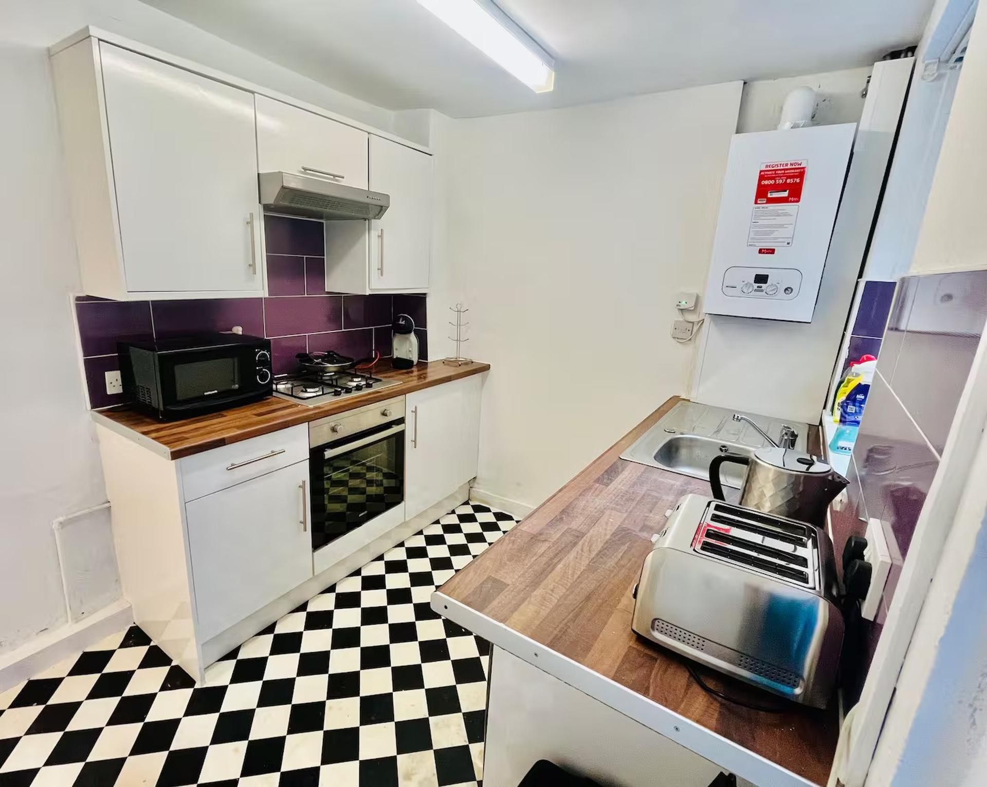 A compact kitchen with white cabinets, a microwave, a gas stove, a toaster, and a checkered floor.