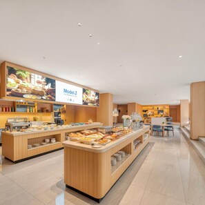 Um moderno buffet de café da manhã com diversas opções de comida e uma tela digital exibindo 'Model J Sua Viagem Confiável'.