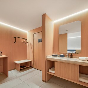Casa de banho moderna com armários de madeira, um banco, pia com produtos de higiene e um espelho.