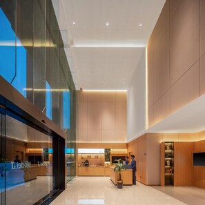Um hall de hotel moderno com balcão de recepção, paredes de vidro e teto alto.