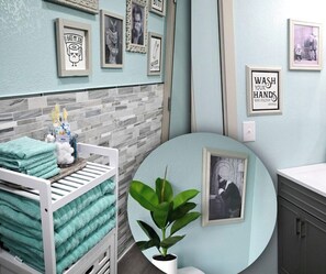 A bathroom with a white bathtub, a sink, and a toilet. There are towels stacked on a rack, a potted plant, and framed pictures on the wall.