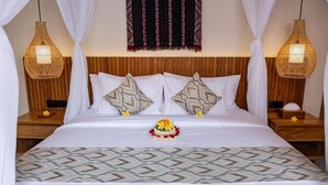 A neatly made bed with a patterned bedspread, two decorative pillows, and a floral arrangement. - Jenna Villa by Genuinehost (Ubud)