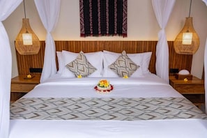 A neatly made bed with a patterned bedspread, two decorative pillows, and a floral arrangement. - Jenna Villa by Genuinehost (Ubud)