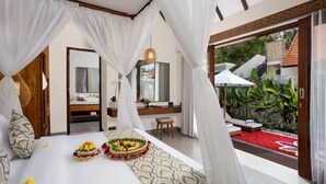 A bedroom with a canopy bed, a small sitting area, and a view of a garden. - Jenna Villa by Genuinehost (Ubud)