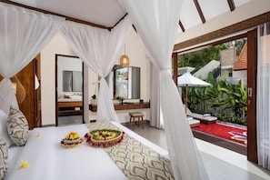 A bedroom with a canopy bed, a small sitting area, and a view of a garden. - Jenna Villa by Genuinehost (Ubud)