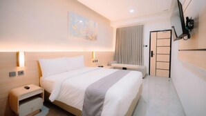 Une chambre d’hôtel avec un lit, des tables de chevet, une télévision et une porte.