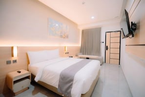 Una habitación de hotel con cama, mesitas de noche, televisor y puerta.