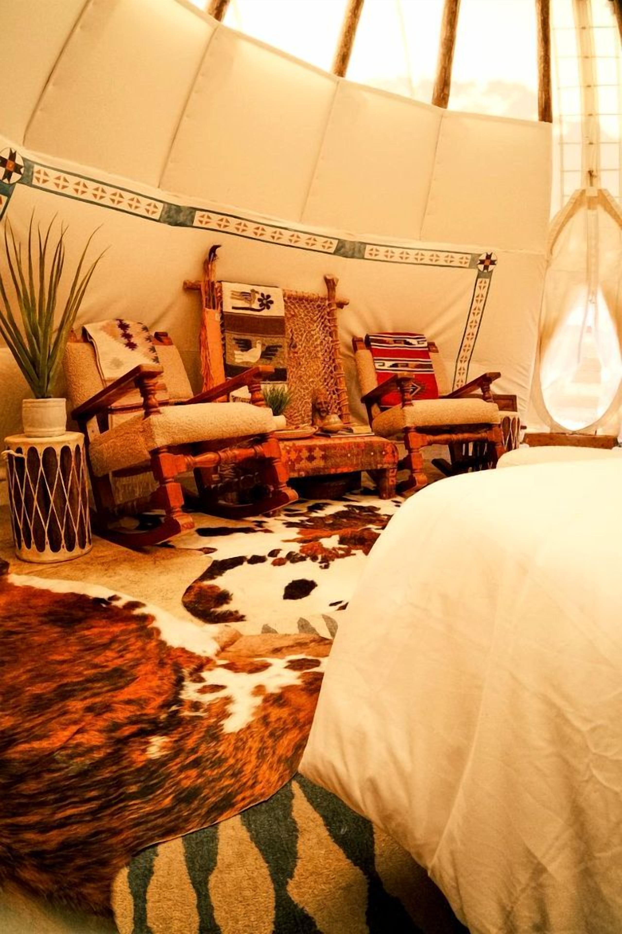 A tent interior with a bed, two rocking chairs, a small table, and a potted plant.