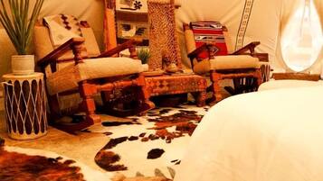 A tent interior with a bed, two rocking chairs, a small table, and a potted plant.