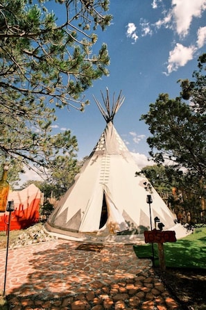 A tipi with a ladder, a stone-paved path, and a sign with the number '050'.