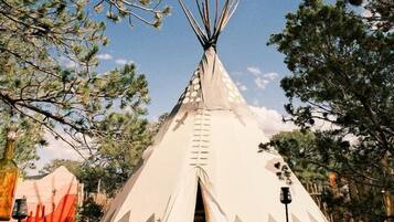 A tipi with a ladder, a stone-paved path, and a sign with the number '050'.