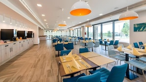 A modern dining area with long tables, blue chairs, and pendant lighting. - Sports Academy Hotel (Balatonfured)