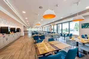 Un'area ristorazione moderna con lunghi tavoli, sedie blu e illuminazione a sospensione.