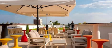 An outdoor seating area with white and orange furniture, a large umbrella, and a view of the sky.