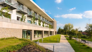 A modern building with multiple balconies, a stone facade, and a well-maintained garden area with pathways and benches. - Sports Academy Hotel (Balatonfured)