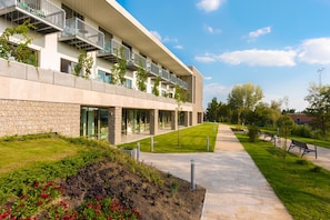 Un edificio moderno con numerosi balconi, una facciata in pietra e un giardino curato con vialetti e panchine.