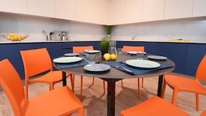 A dining area with a round table, orange chairs, and a kitchen in the background. - Yugo Lee Point (Cork)