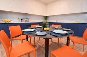 A dining area with a round table, orange chairs, and a kitchen in the background. - Yugo Lee Point (Cork)