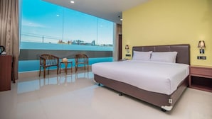 A hotel room with a large bed, a view of the city, and a balcony with chairs. - RAV Hotel (Tanjung Pinang)