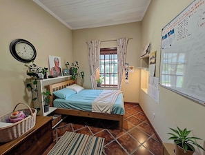 Ein Schlafzimmer mit einem Bett, einer Uhr, einem Fenster mit Vorhängen, einer Whiteboard-Tafel und einer Zimmerpflanze.