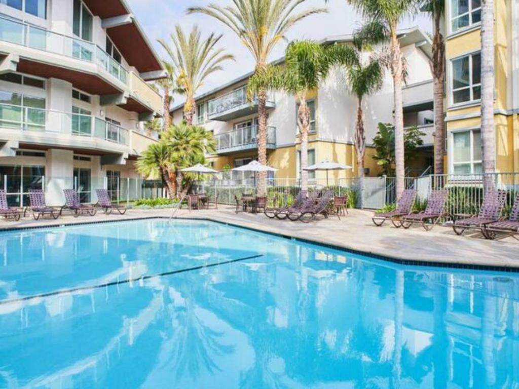 A swimming pool with lounge chairs and palm trees, surrounded by multi-story buildings.