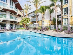 A swimming pool with lounge chairs and palm trees, surrounded by multi-story buildings. - The Solace - Peaceful Garden Side View Pool Gym (Marina del Rey)