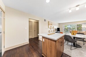 A modern kitchen with a wooden island, a dining area with a table and chairs, and a large window with a view. - The Solace - Peaceful Garden Side View Pool Gym (Marina del Rey)