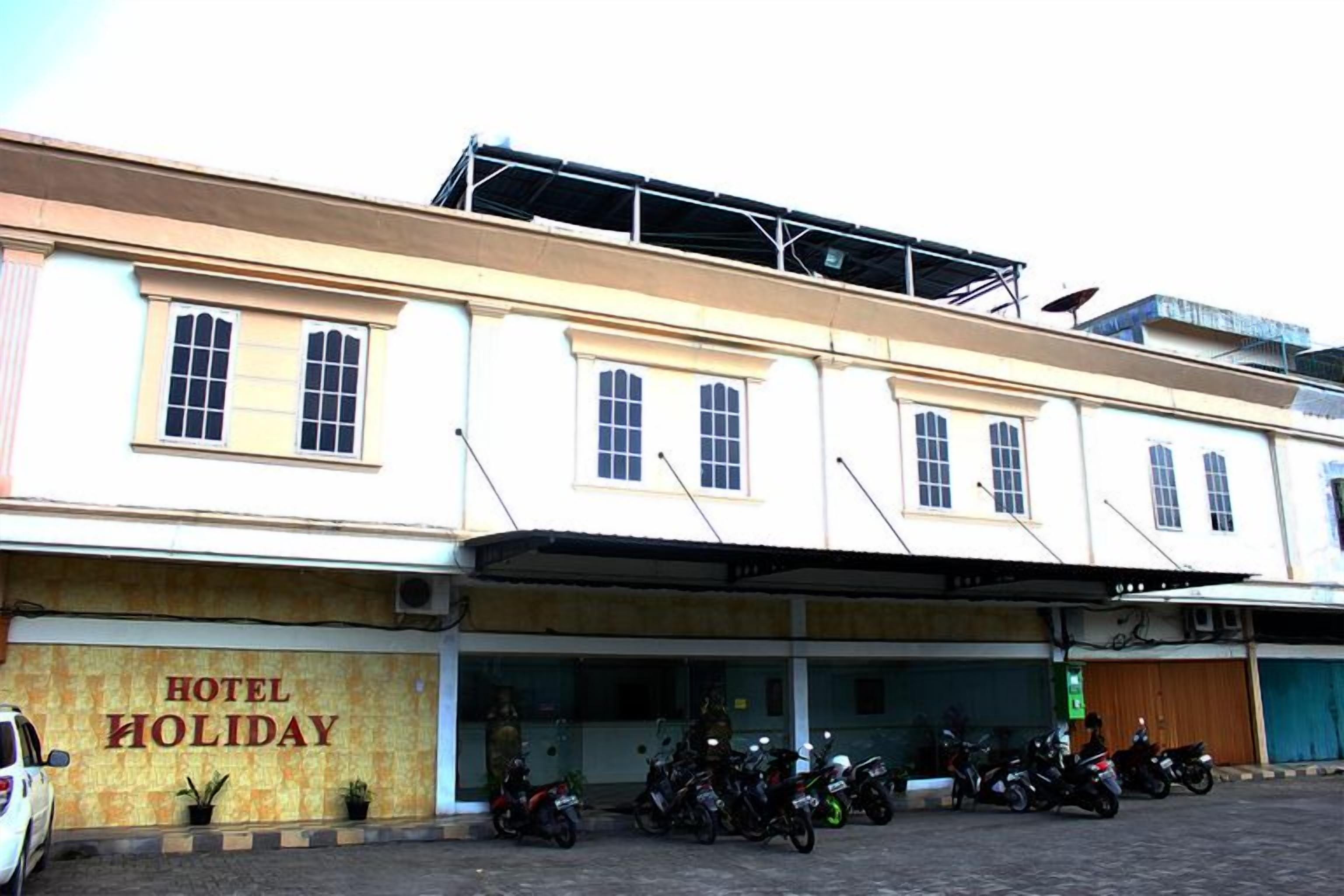 A building with a sign reading 'HOTEL HOLIDAY' and a row of parked motorcycles in front.