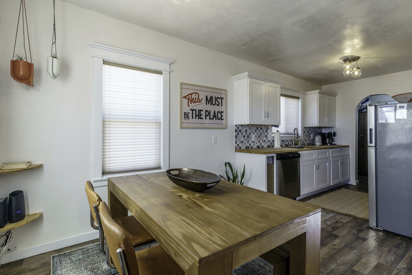 A modern kitchen with white cabinets, a wooden dining table, and a stainless steel refrigerator.