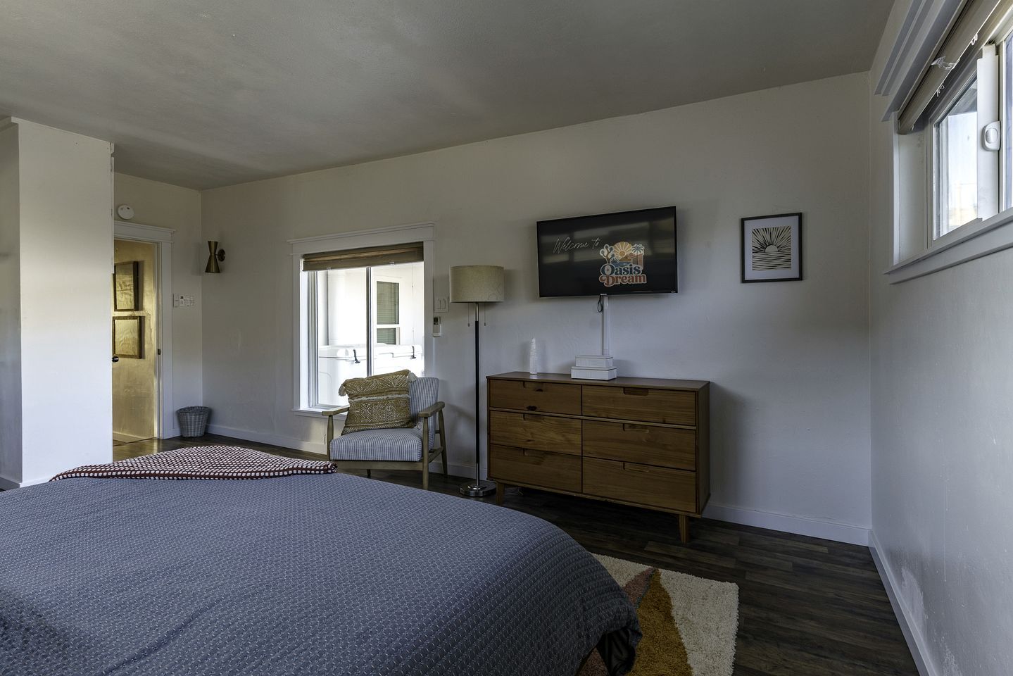 A bedroom with a bed, a dresser, a chair, a lamp, and a television on the wall.