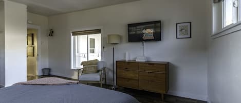 A bedroom with a bed, a dresser, a chair, a lamp, and a television on the wall.