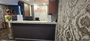 Un mostrador de recepción de hotel con diseño moderno, un cartel que dice 'ENRICH HOTEL' y una pared decorativa con motivos florales.
