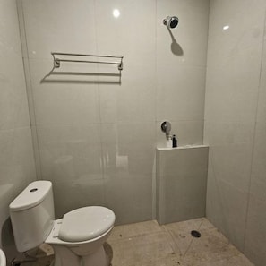 A small, enclosed bathroom with a toilet, a shower, and a sink. - Bell Hotel Merauke (Merauke)