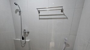 A small, tiled bathroom with a shower, toilet, and a small sink. - Bell Hotel Merauke (Merauke)