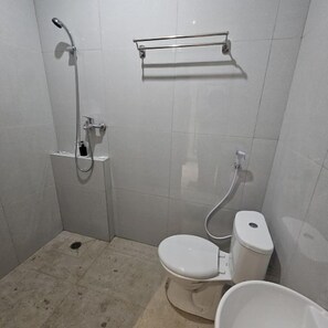 A small, tiled bathroom with a shower, toilet, and a small sink. - Bell Hotel Merauke (Merauke)