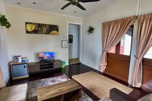 Una sala de estar con televisión de pantalla plana, ventilador de techo y un ventanal con cortinas.
