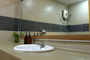 Un baño con un lavamanos blanco, un espejo, un cabezal de ducha manual y un dispensador de jabón.