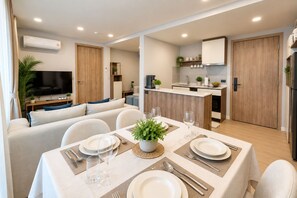 Uma sala de estar moderna com sofá, mesa de jantar para dois e área de cozinha com bancada e armários.