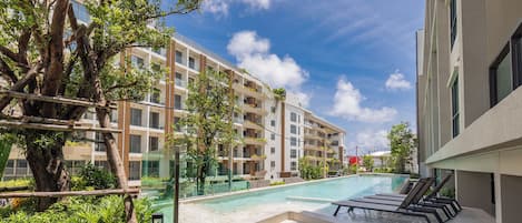 A modern hotel with a swimming pool, surrounded by lush greenery and a clear blue sky.