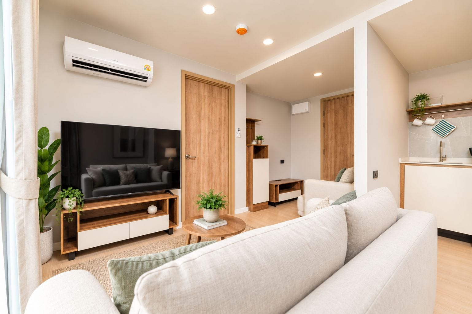 Een moderne woonkamer met een flatscreen televisie, een bank, een salontafel, en een keukenhoek met een spoelbak en kastjes.