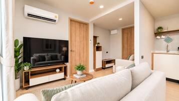 Een moderne woonkamer met een flatscreen televisie, een bank, een salontafel, en een keukenhoek met een spoelbak en kastjes.
