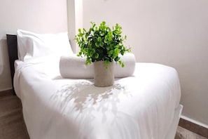 Una cama con ropa de cama blanca y una planta en maceta.
