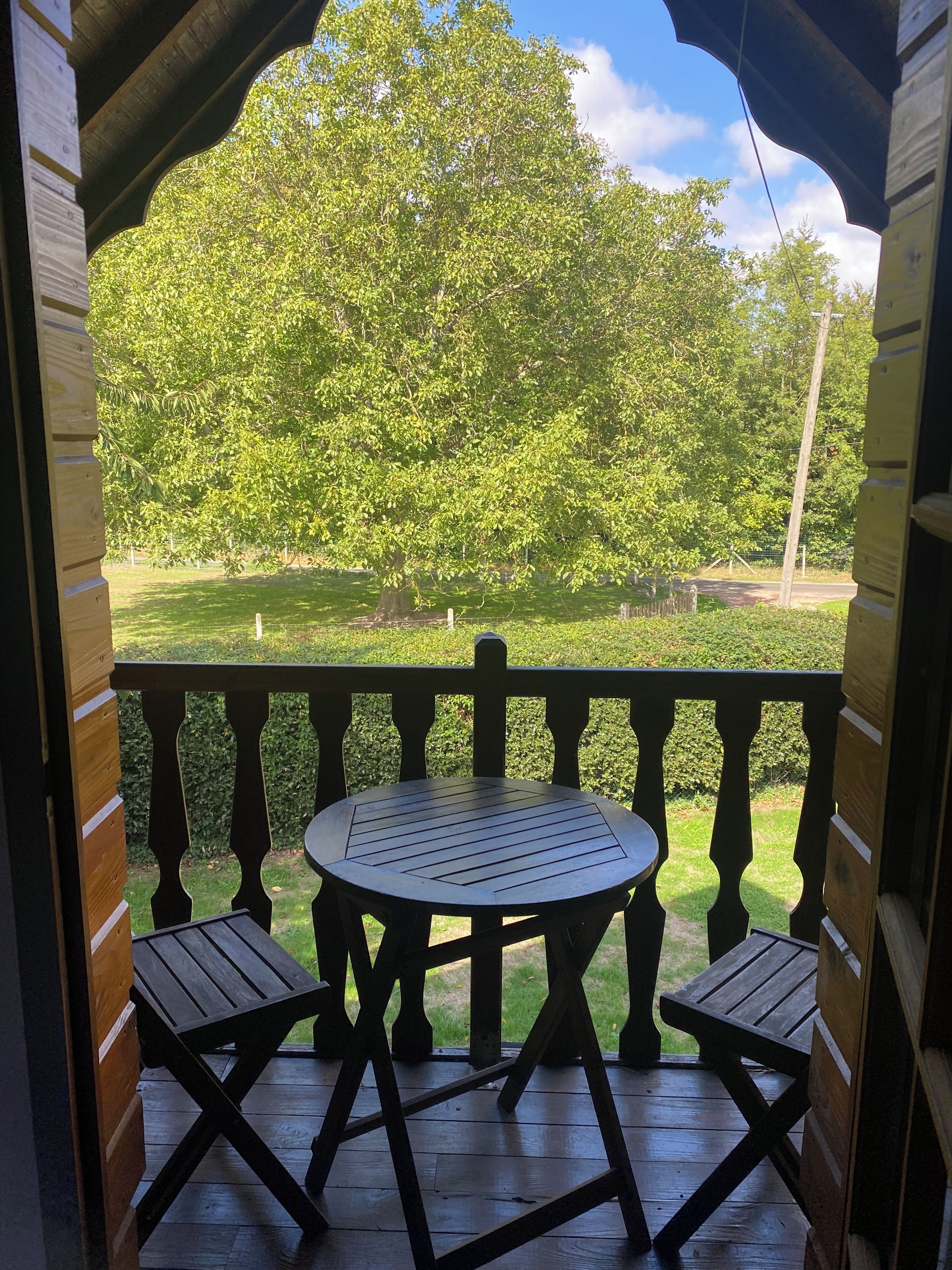 Une terrasse en bois avec une table ronde et deux chaises, donnant sur un espace verdoyant bordé d’arbres.
