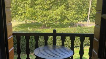 Une terrasse en bois avec une table ronde et deux chaises, donnant sur un espace verdoyant bordé d’arbres.