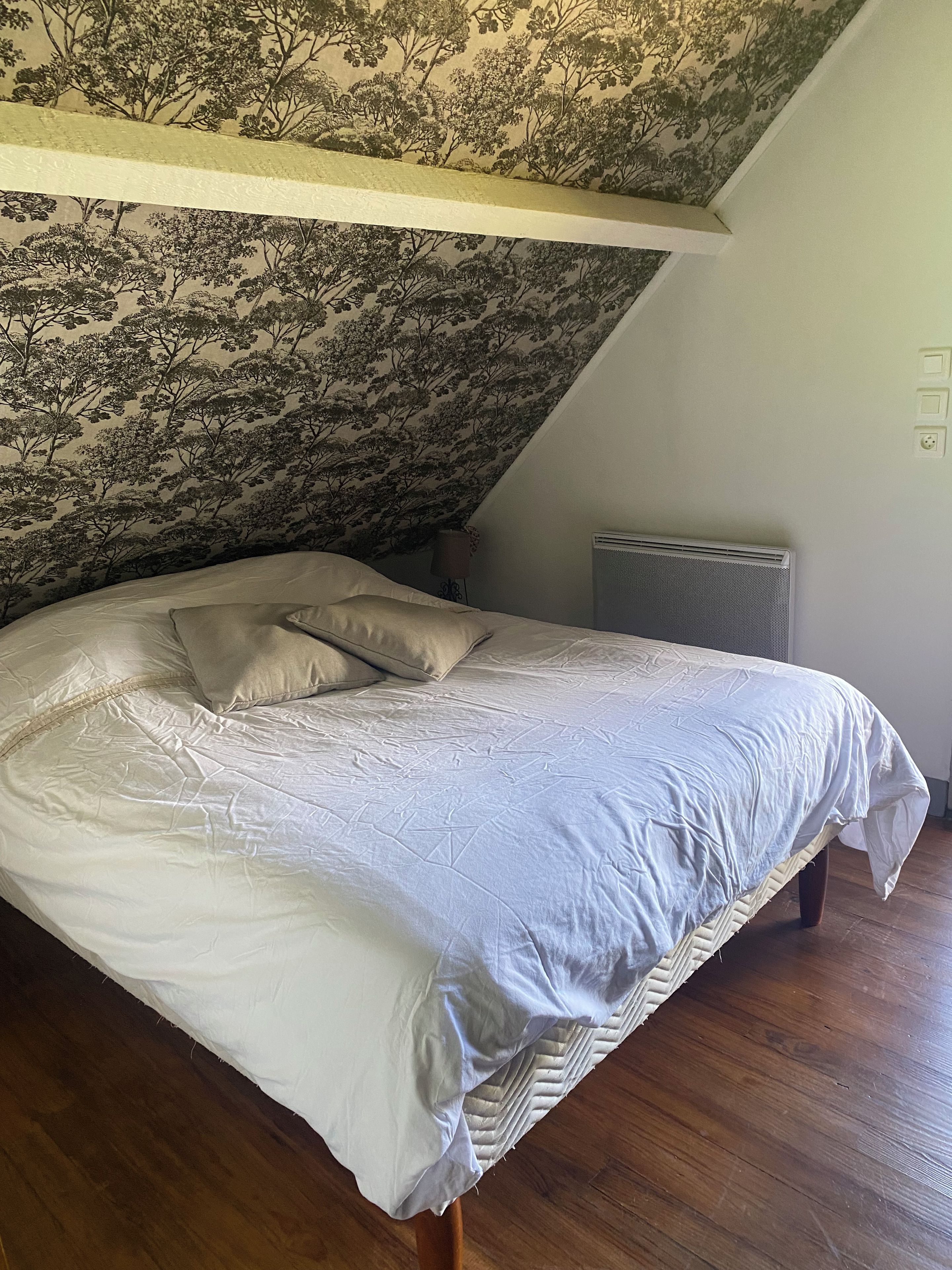 Une chambre à coucher avec un lit, un radiateur et un mur orné d’un motif floral.