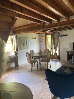 A dining area with a wooden ceiling, a table with chairs, a painting on the wall, and a window with curtains.