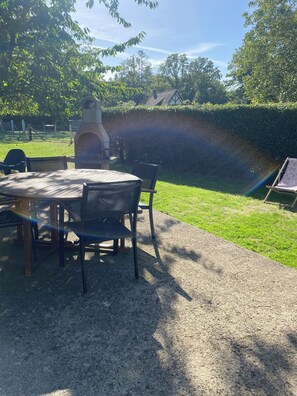 An outdoor patio with a round table and chairs, a barbecue grill, and a view of a rainbow.